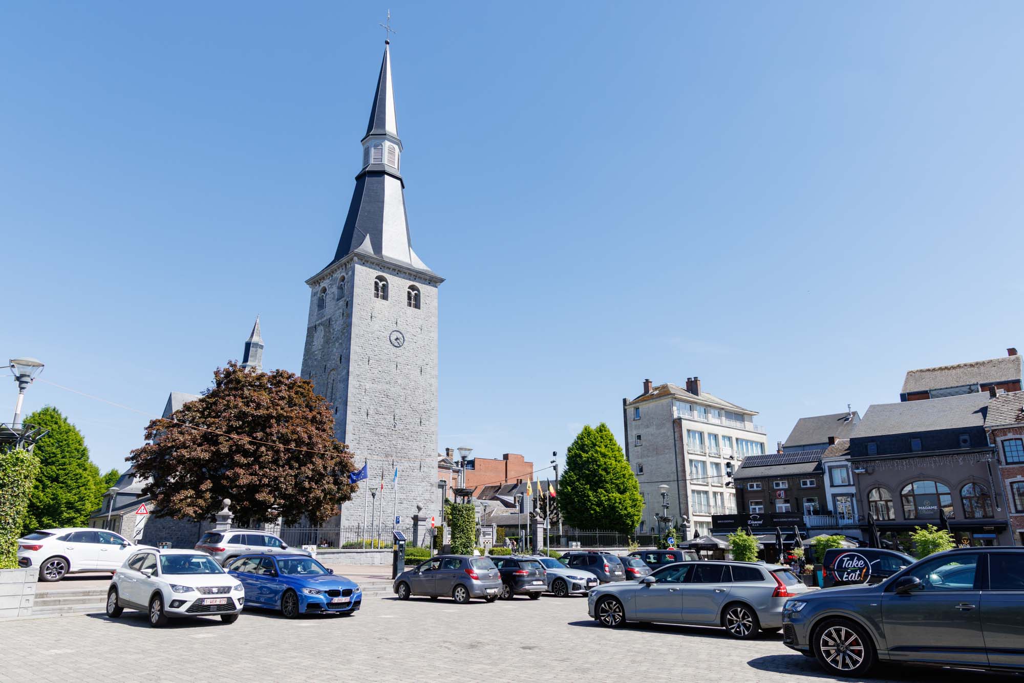 Toren van de Sint-Niklaaskerk en het centrale plein van Ciney bij zonnig weer.