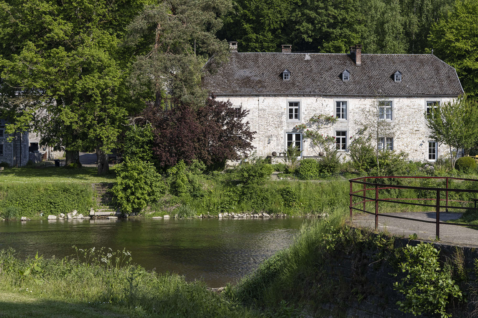 Natuurstenen huizen langs de rivier in Hamoir, omringd door groen met een klein bruggetje en rustige sfeer.