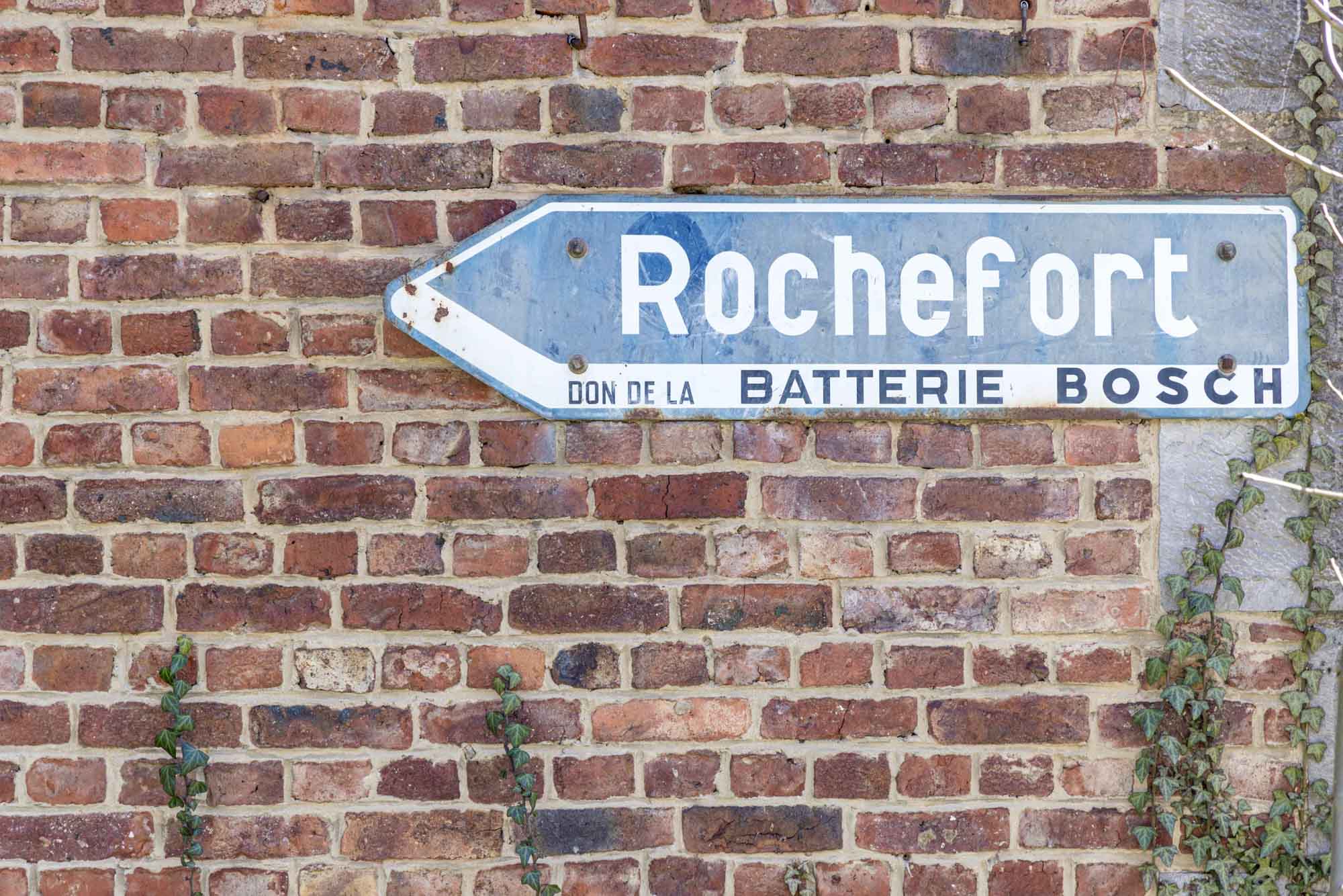 Blauw bord met de aanduiding Rochefort, bevestigd op een oude bakstenen muur.