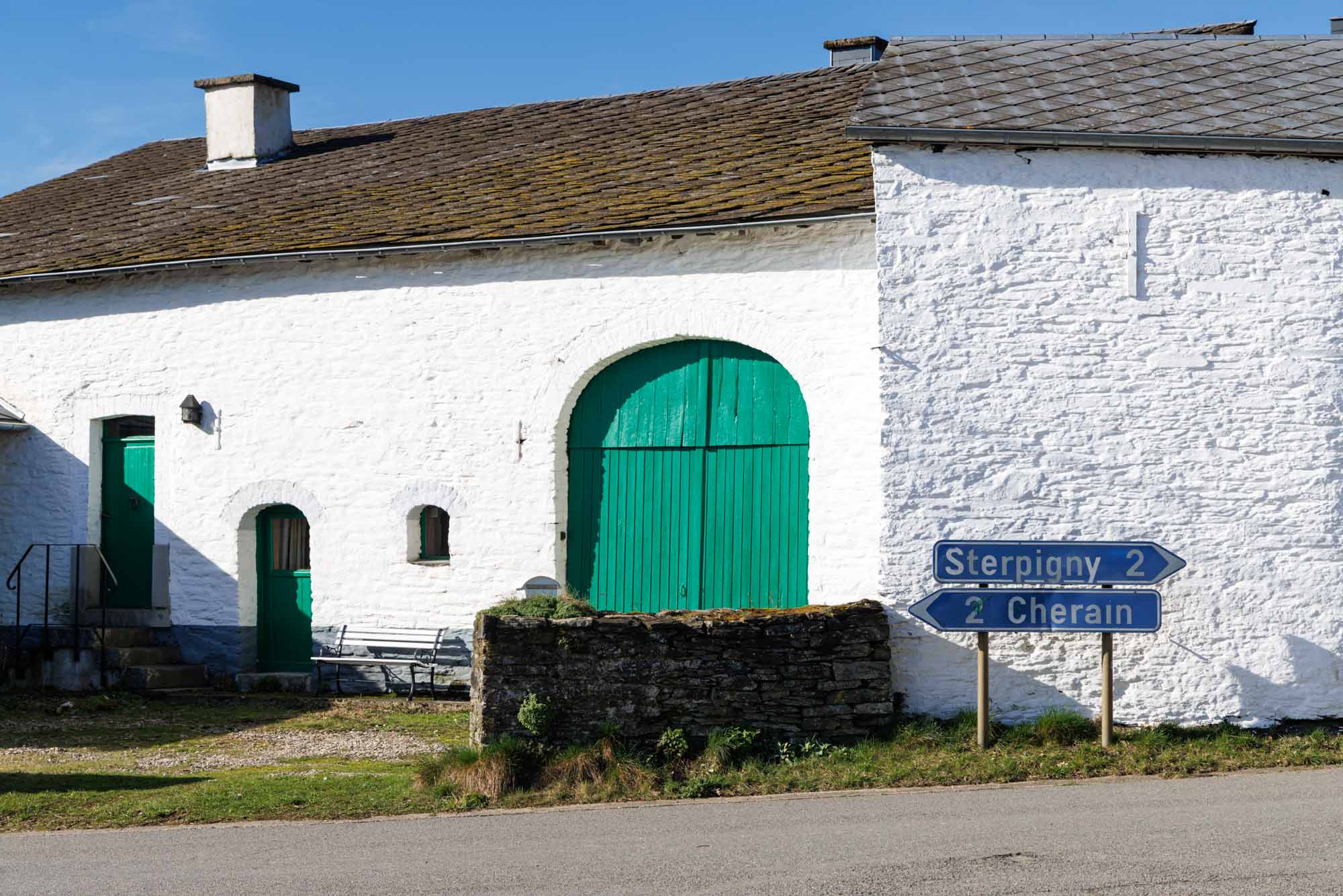 Wit stenen huis in Rettigny met groene deur en wegwijzer langs de weg