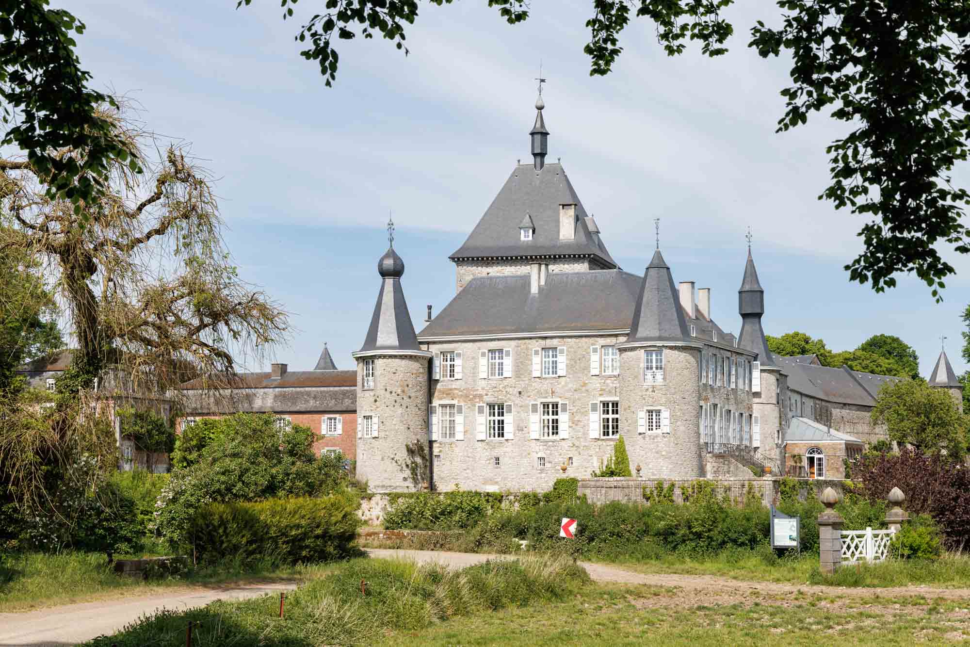 Château d’Hodoumont omringd door groen, met stenen gevels en torens onder een heldere hemel.