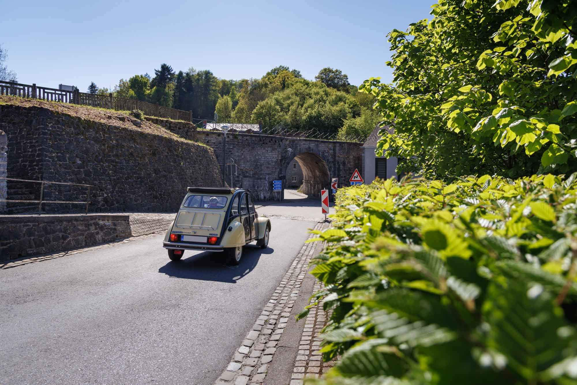 Sosoye met 2CV richting gewelfde doorgang omgeven door groen