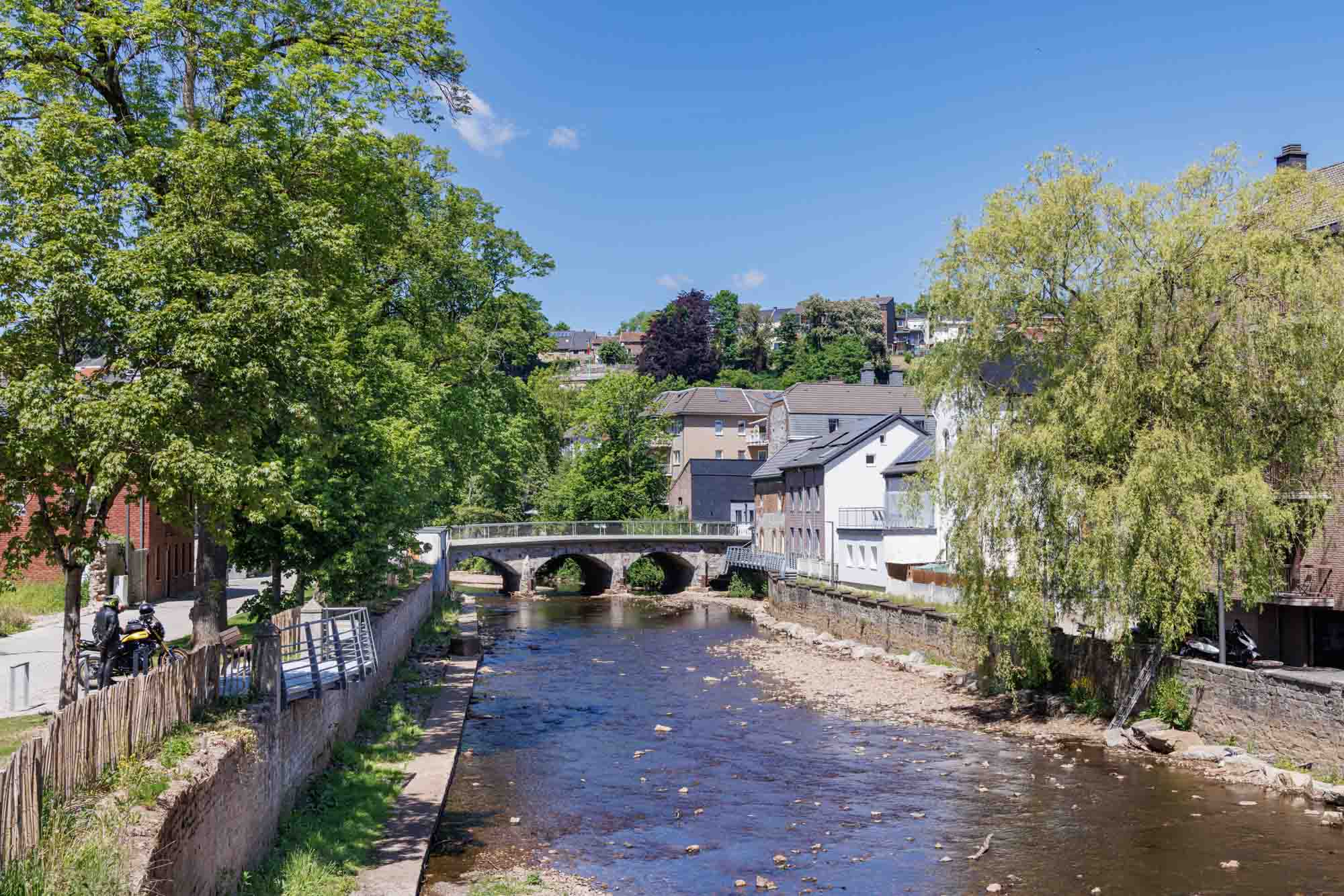 De Vesder in Eupen met een stenen brug, huizen langs de rivier en zomerse begroeiing.